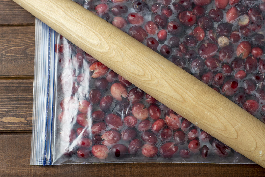 A plastic storage bag filled with fresh cranberries and a rolling pin resting on top of the bag. 
