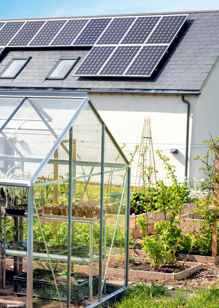 A greenhouse is shown next to a garage with several rows of solar panels on the roof.