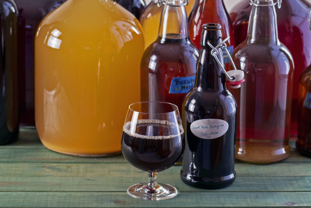 Bottles and jugs of different homebrews with a glass of beer and an open bottle next to it. 