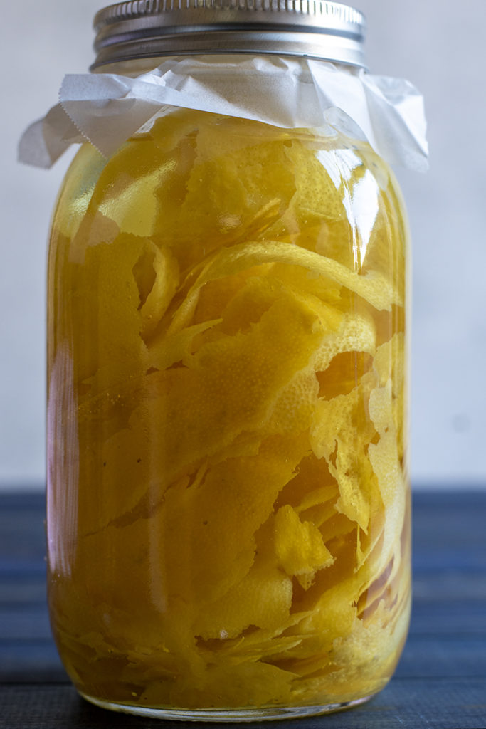 Close up of a jar filled with vodka and lemon peels.