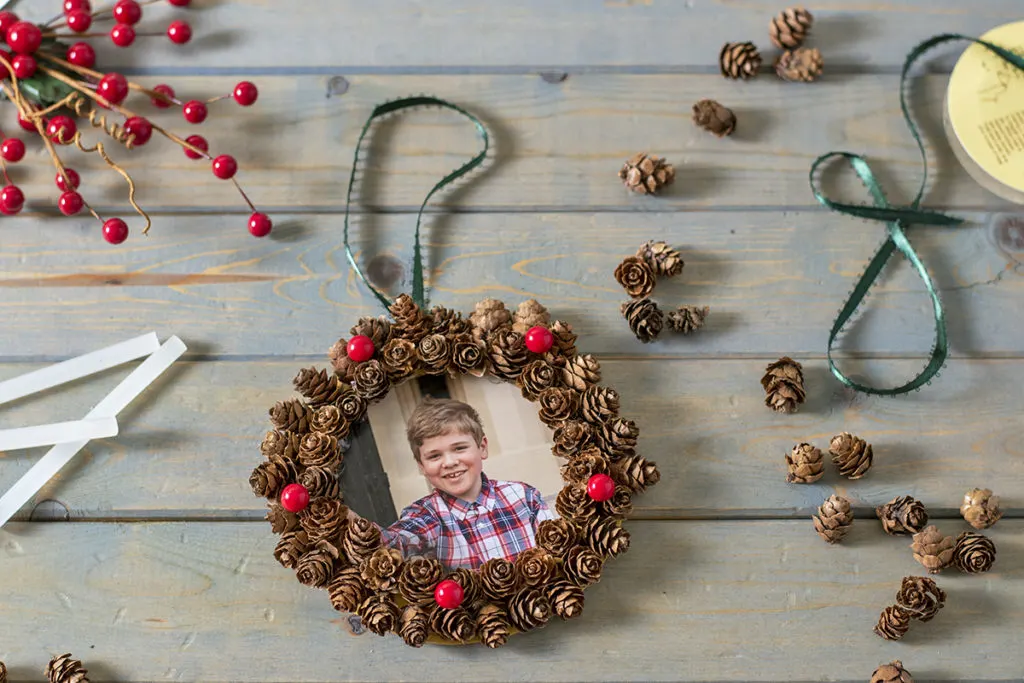 A child's picture is ringed with hemlock cones to make a Christmas ornament.