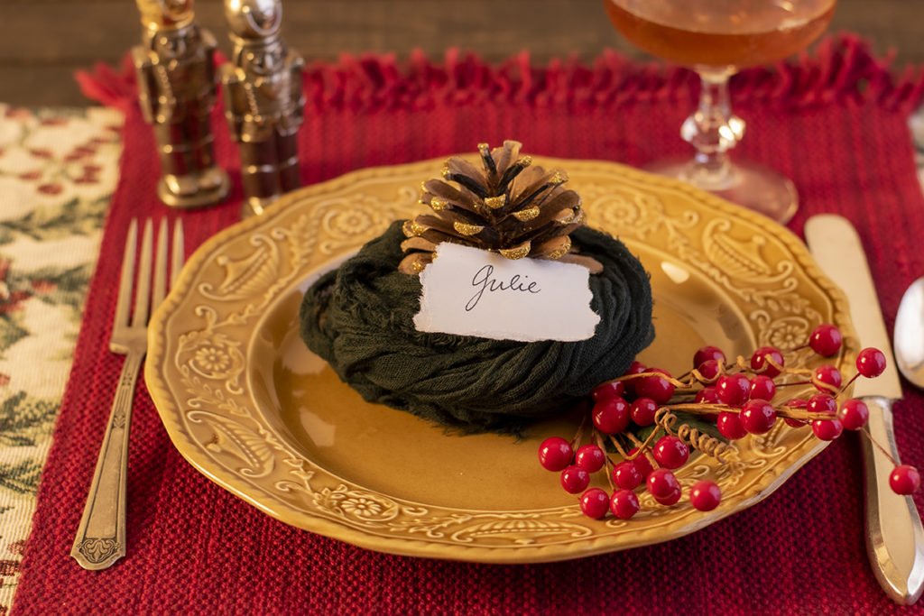 Christmas dinner place setting with pine cone place card holder.