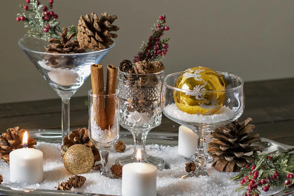 A decorative display of pine cones, candles, Christmas ornaments, and glasses.