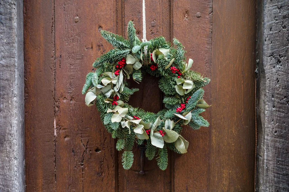 An evergreen wreath is hanging in front of a door. 