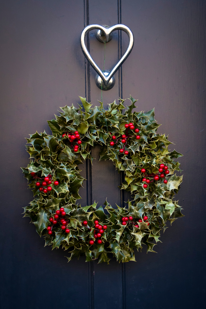 A wreath made of holly hangs on a door.