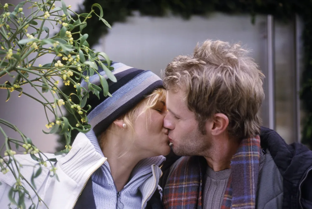 A couple kissing under mistletoe outside.