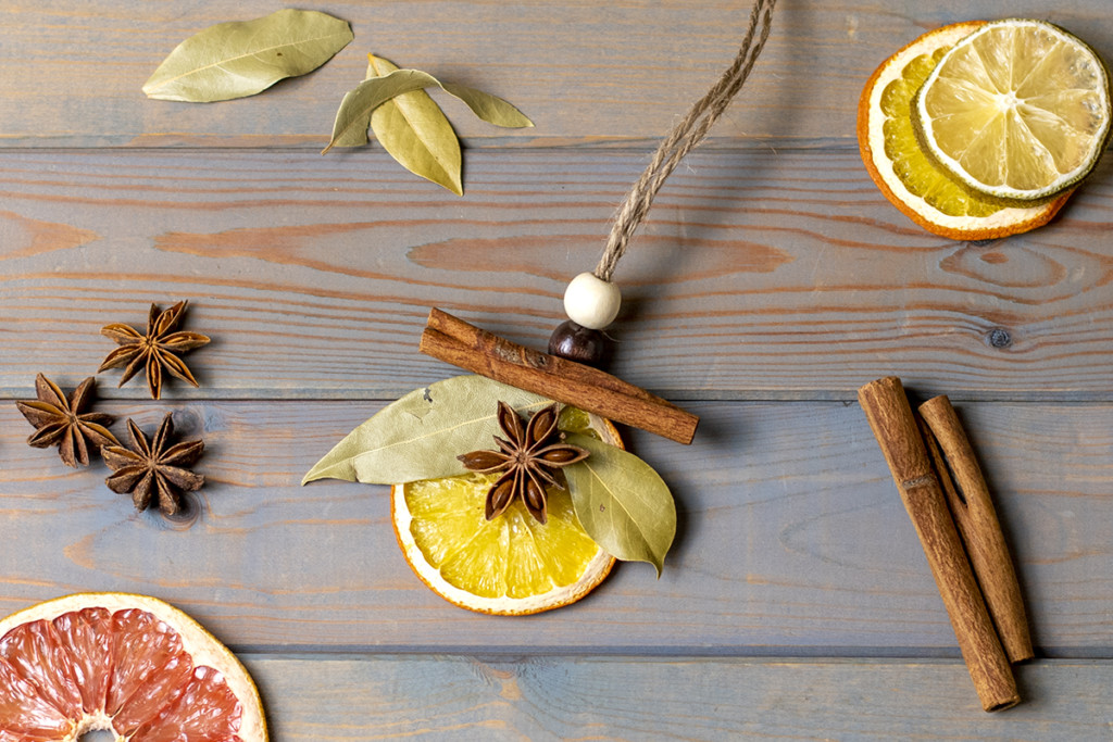 Spices and dried orange slices surround an ornament made from a dried orange slice. It has been decorated with wooden beads, a cinnamon stick, bay leaves, and a star anise.