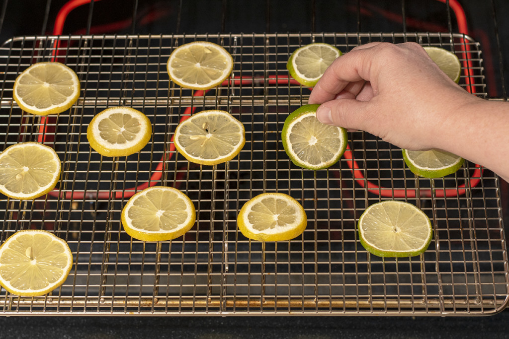 A hand is show flipping over lemon slices drying in an oven.