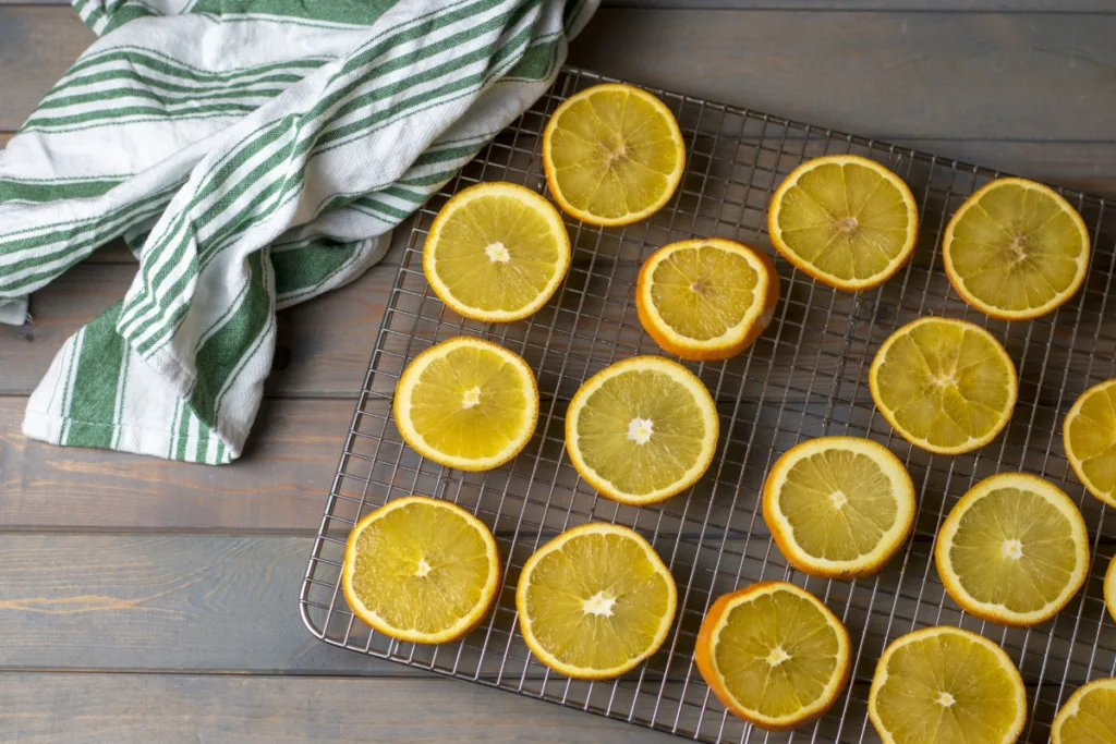 Fresh orange slices arranged on a drying rack. A green striped kitchen towel is next to the drying rack.