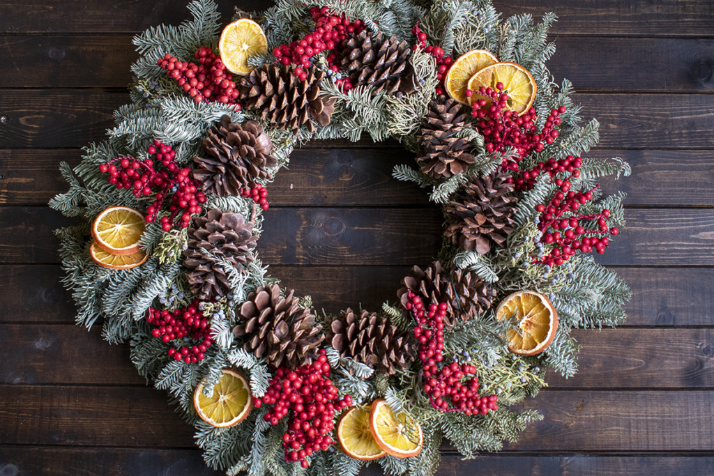 a large Christmas wreath made of evergreens, pinecones, juniper, red berries and dried orange slices.