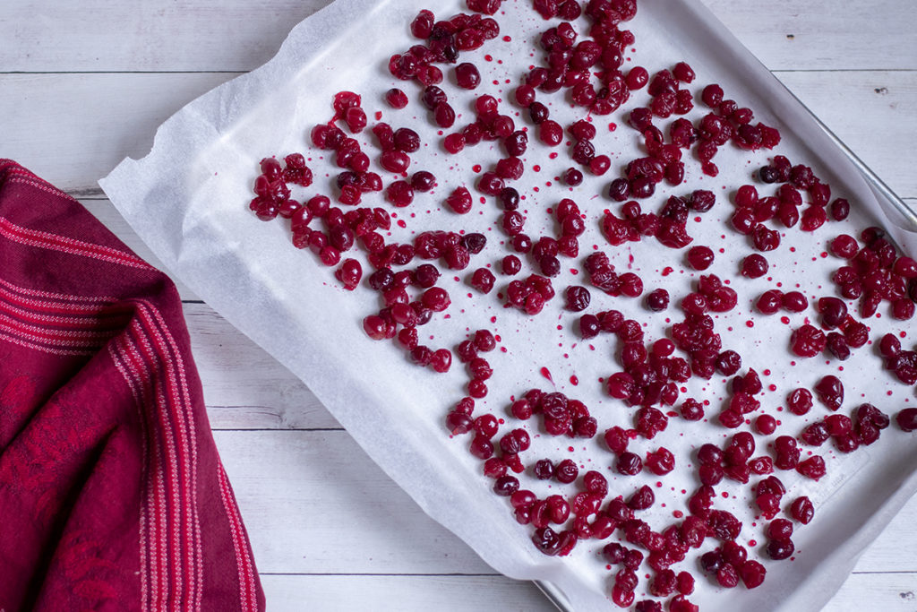 A parchment-lined baking sheet with cider-cooked cranberries spread on it.