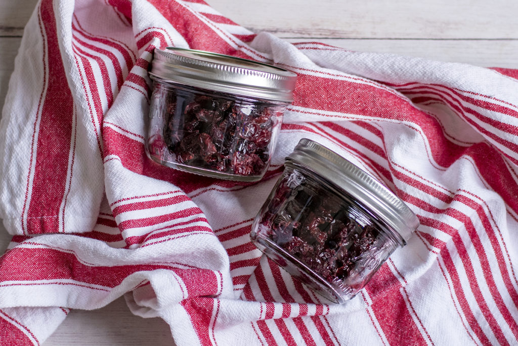 Two small jars filled with homemade dried cranberries displayed on a red and white striped towel.