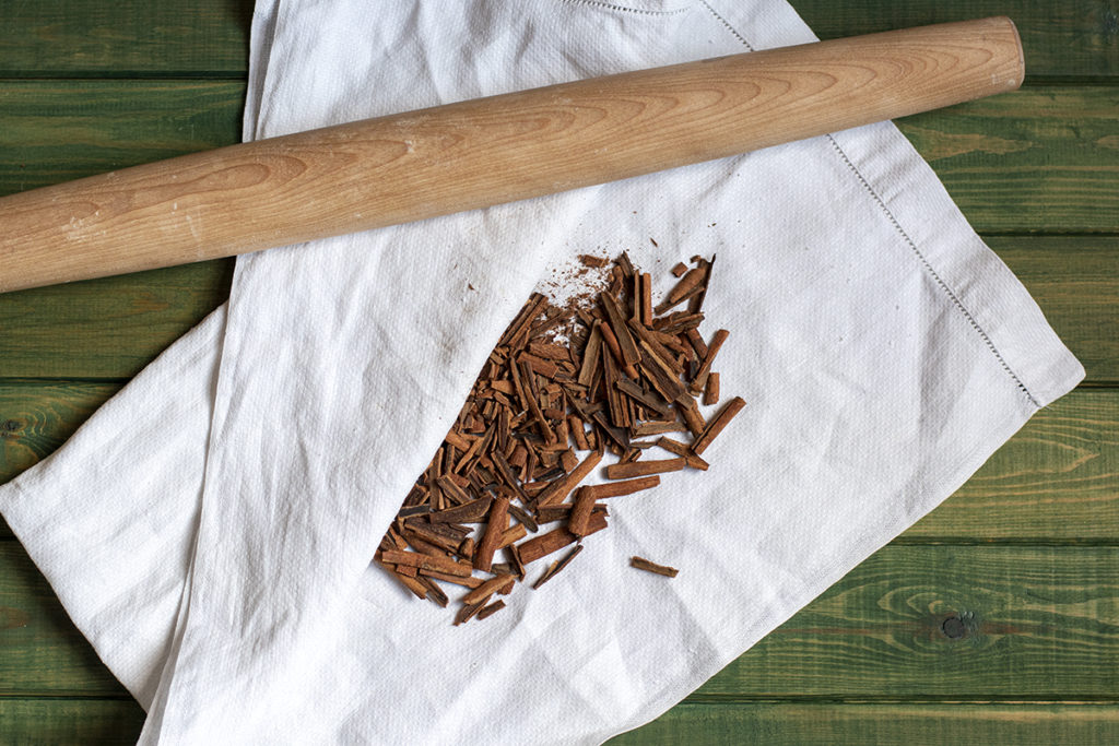 Crush cinnamon sticks on a white tea towel. A French rolling pin rests near the tea towel. 