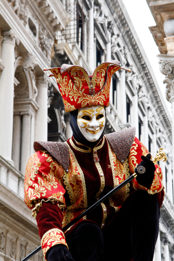 Someone wearing a court jester costume with a mask and cane.