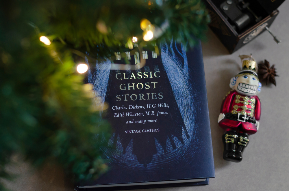 A book of ghost stories is set under a Christmas tree next to a nutcracker ornament.