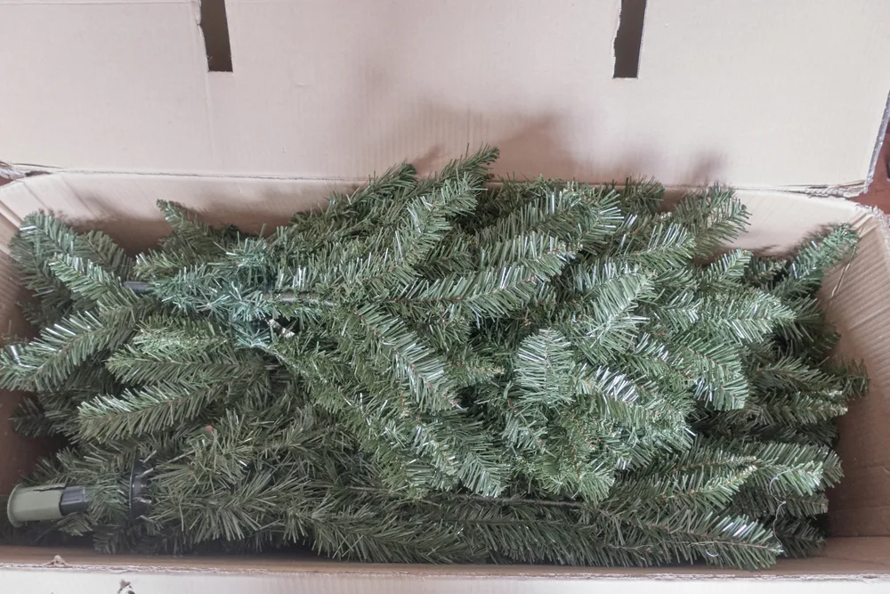 An artificial Christmas tree in pieces packed in a cardboard box.