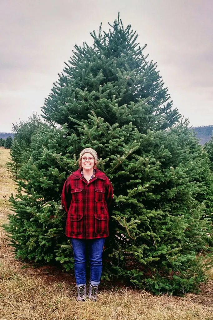Writer, Tracey Besemer, smiling and standing in front of a twelve foot tall Frasier fir.