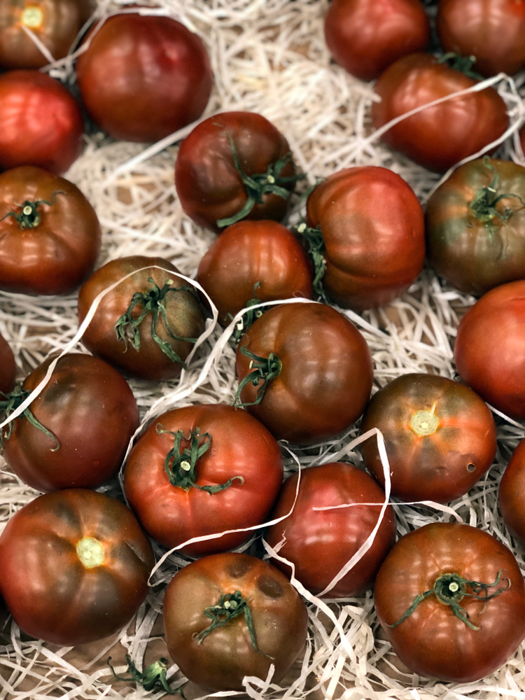 Black Prince tomatoes set on a paper bag with bits of straw.