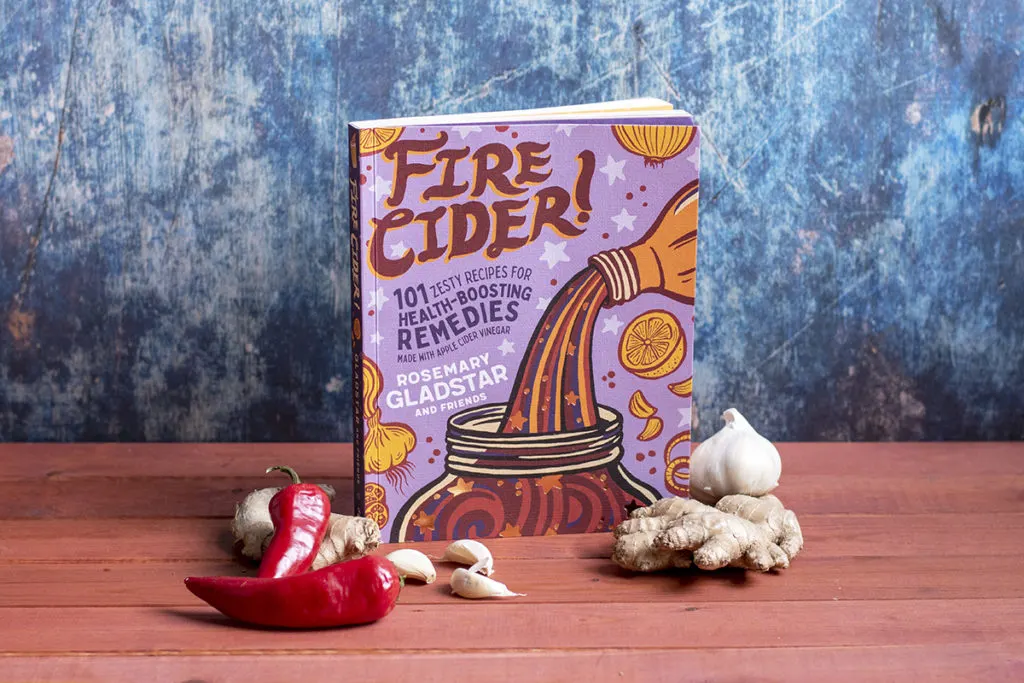 The book, " Fired Cider" by Rosemary Gladstar and Friends is shown with fire cider ingredients sitting next to it. 