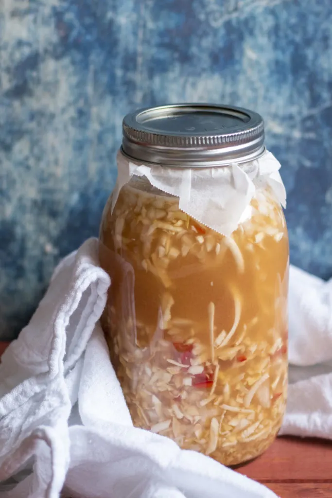 A jar of fire cider ingredients wrapped in a white linen towel against a blue background.