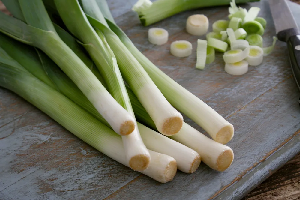 Washed leeks on a cutting board with a knife. One leek has been sliced.