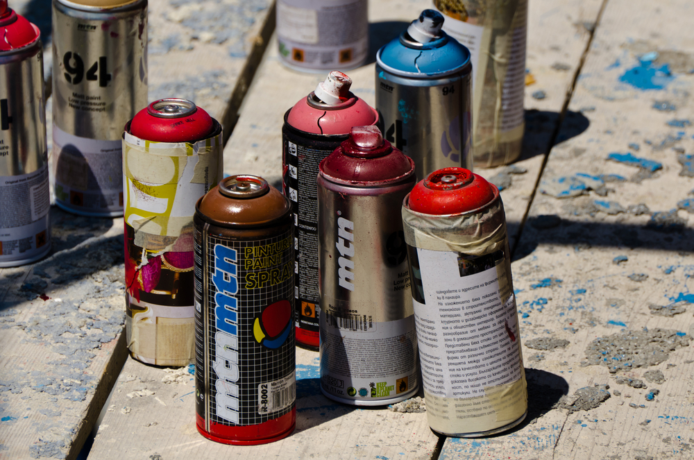 Several spray paint cans on wooden floor boards in the sun.