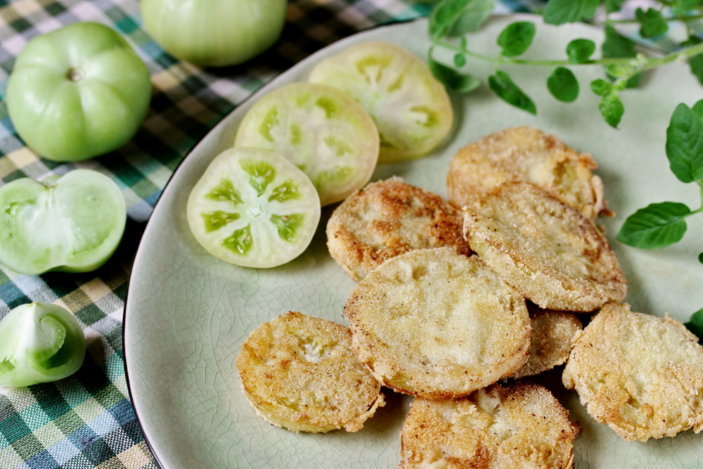 A plate of fried green tomatoes next to raw green tomatoes. 