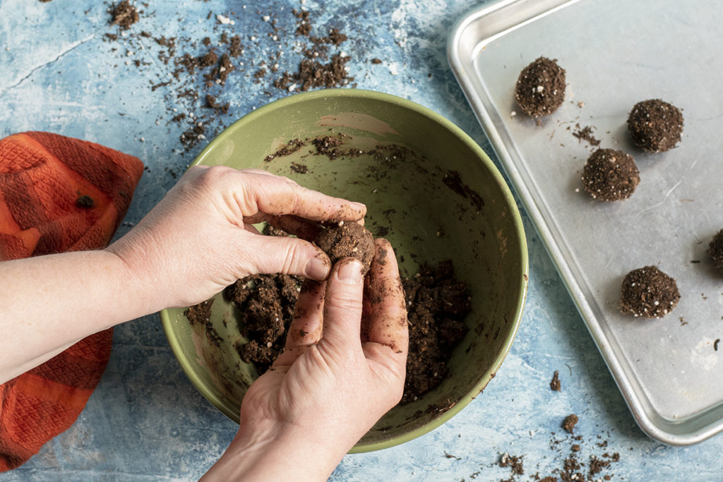 A woman's hands are rolling wildflower bomb dough into a bowl.