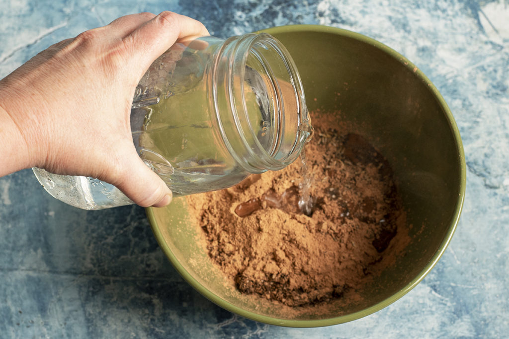A hand is pouring water from a mason jar into a bowl of clay and potting mix.
