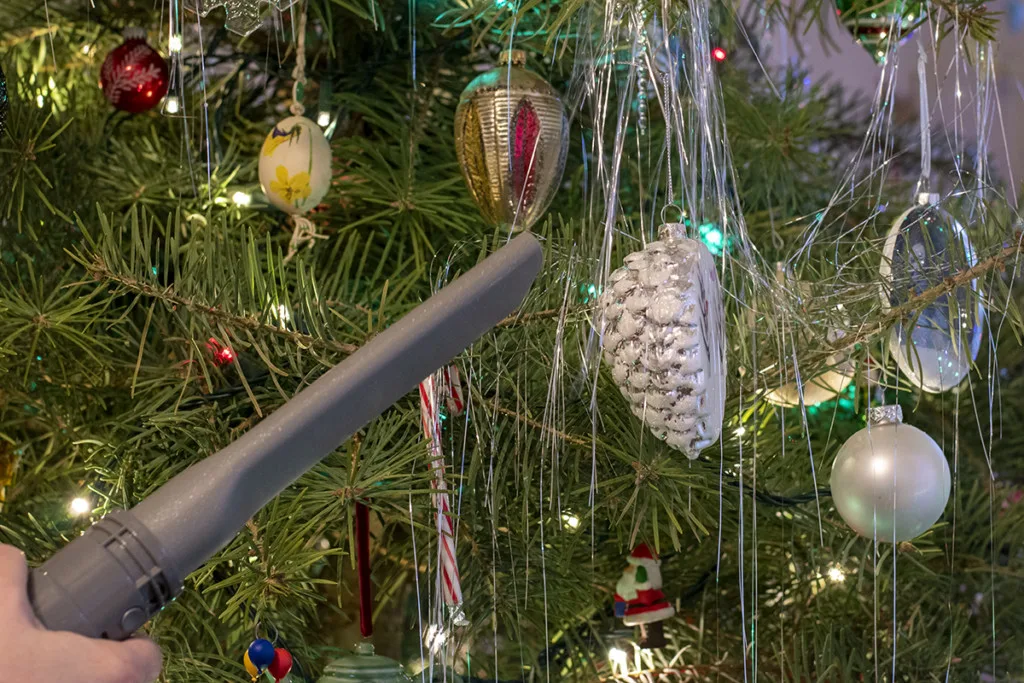 A vacuum cleaner nozzle hovers near an ornament and tinsel on a Christmas tree.