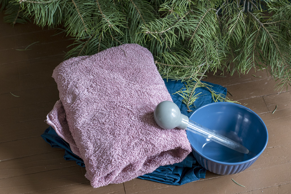 A blue king-size sheet, an old towel, a bowl and a turkey baster are set at the foot of an undecorated Christmas tree.