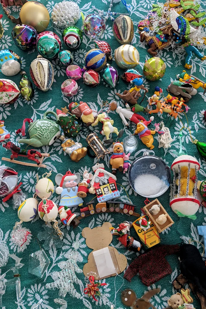 A table is covered with an assortment of Christmas ornaments removed from the tree.