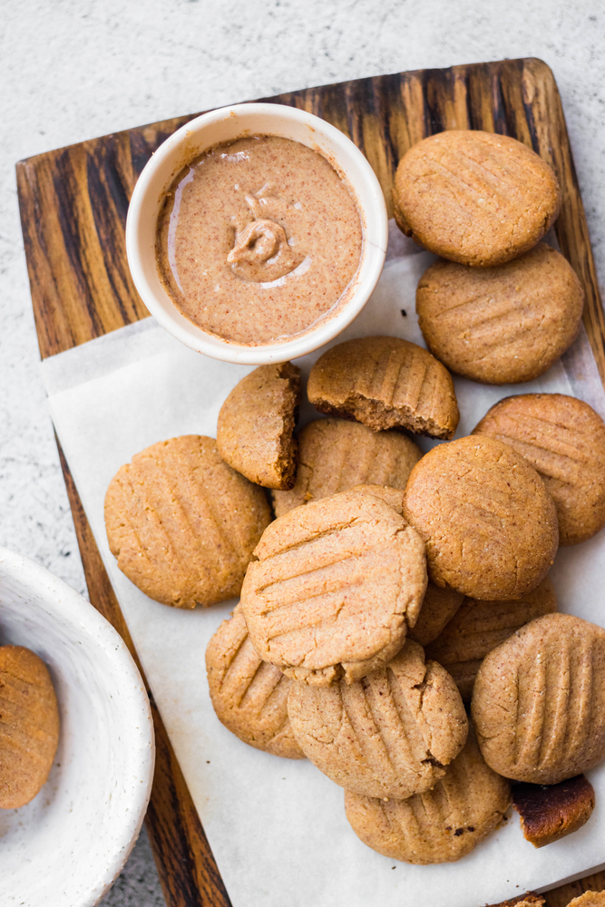 A ramekin with nut butter next to freshly baked peanut butter cookies. 