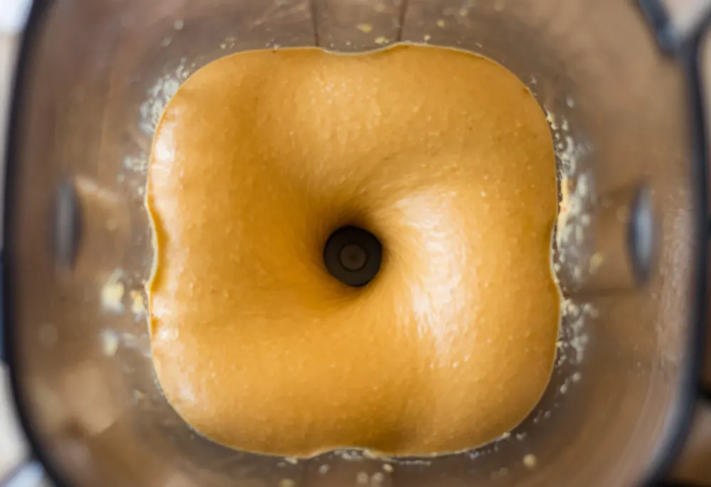 A close up of a blender jar with blended peanut butter. 
