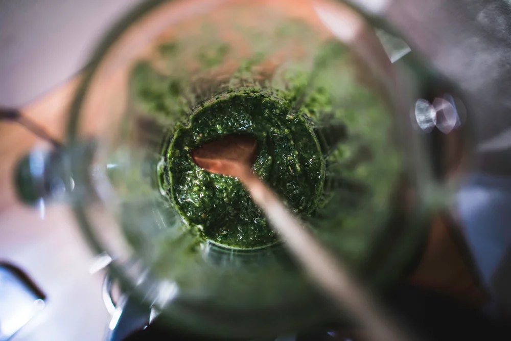 A close up of pest in a blender jar with a wooden spoon in it.