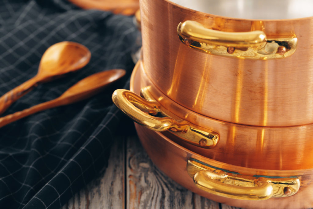A stack of copper pots and pans next to a dish towel and wooden spoons.