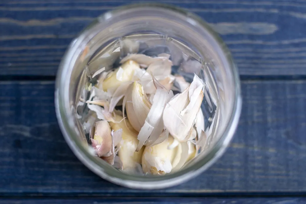 A jar of partially peeled garlic cloves sitting on a blue wooden background.