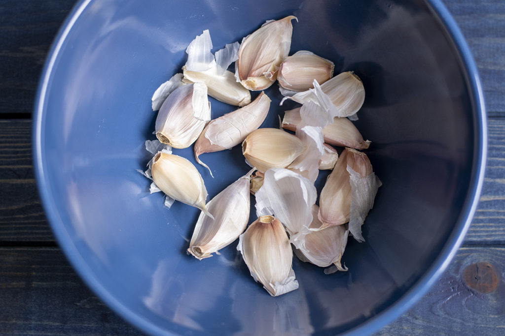 A blue bowl with the cloves from a bulb of garlic.