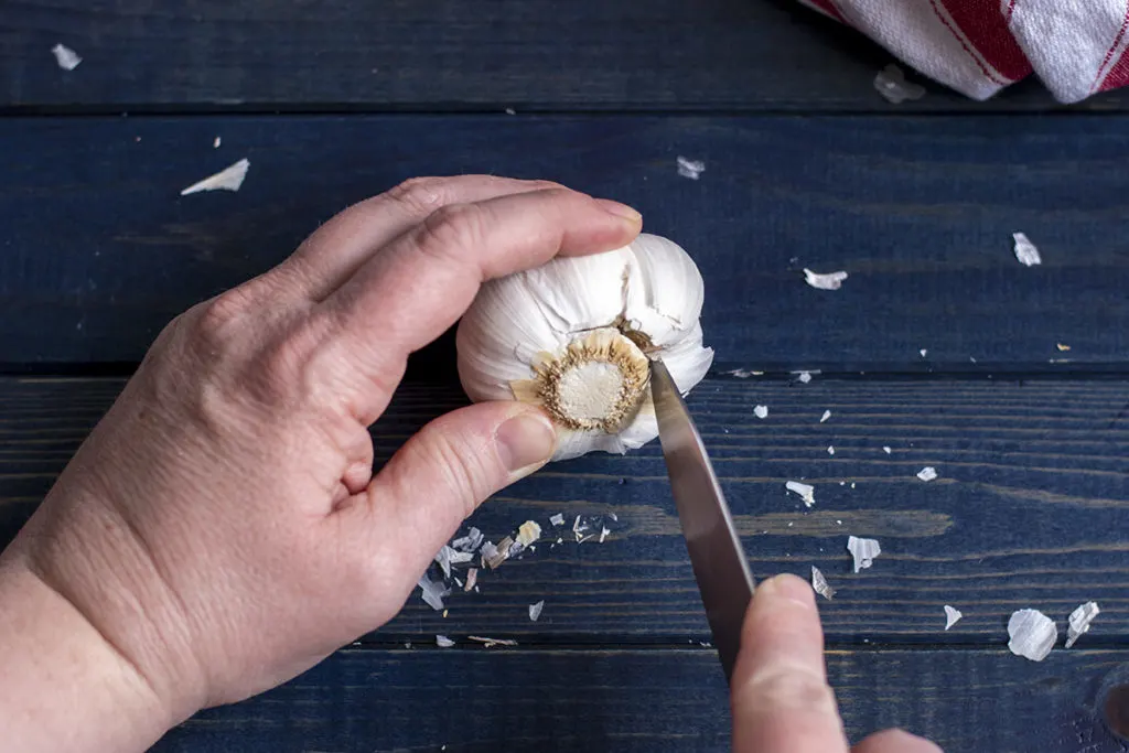 Hands cutting the base of a clove of garlic. 