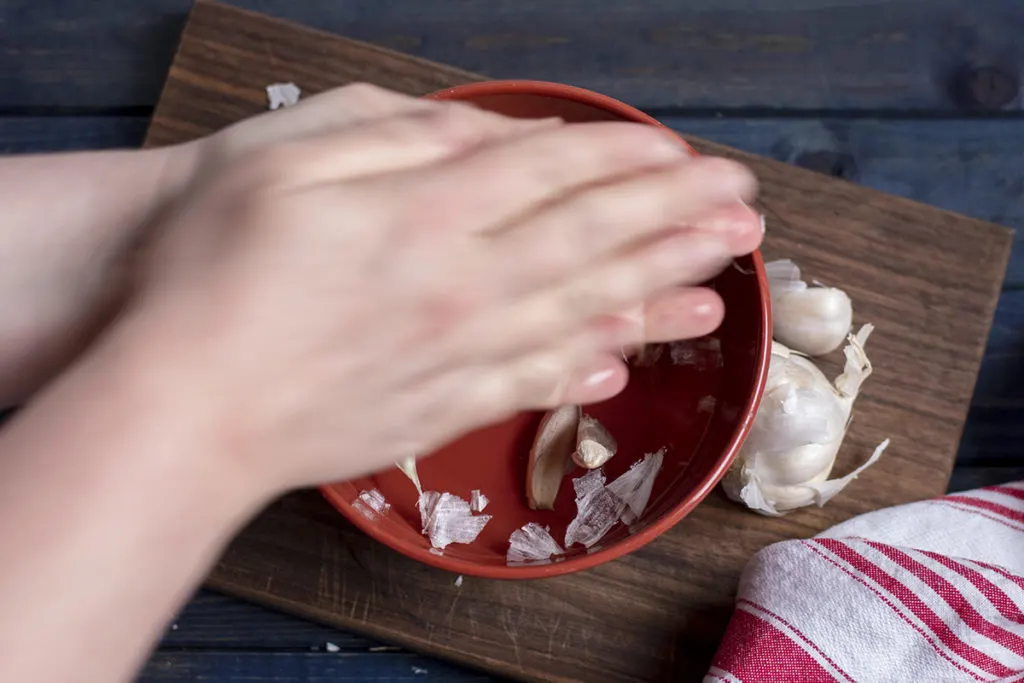 My blurred hands rubbing garlic cloves together over the bowl of water.