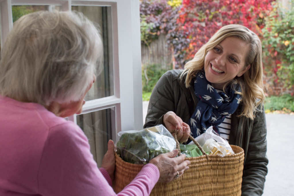 Woman handing basket full of groceries to an elderly neighbor.
