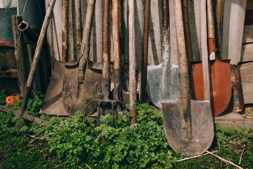 A row of old garden tools leaning up against a shed.