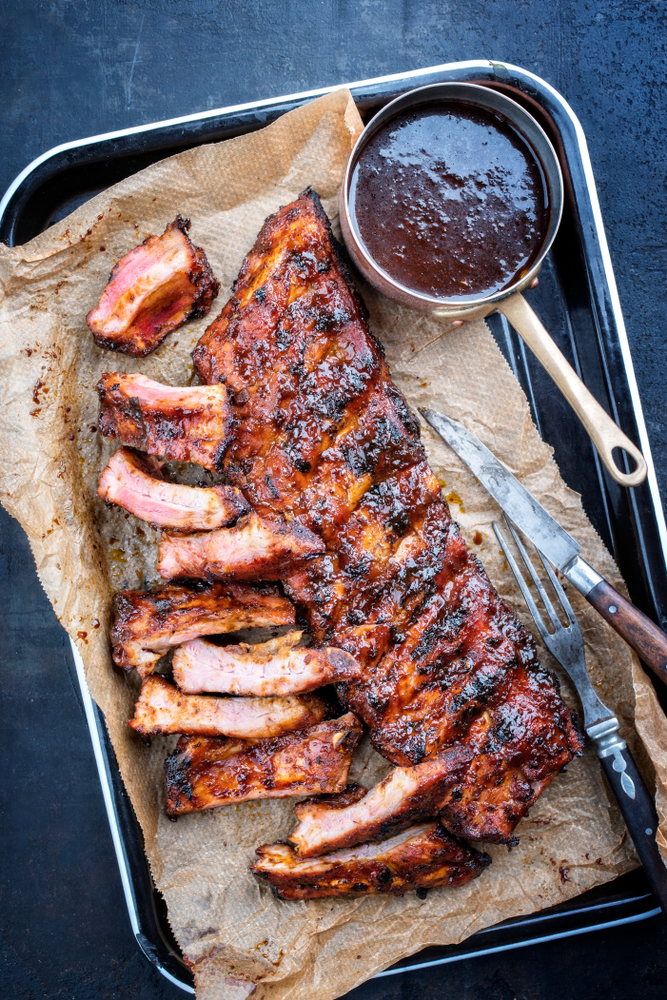 A pan of ribs with a small pot of maple syrup barbecue sauce next to it. 