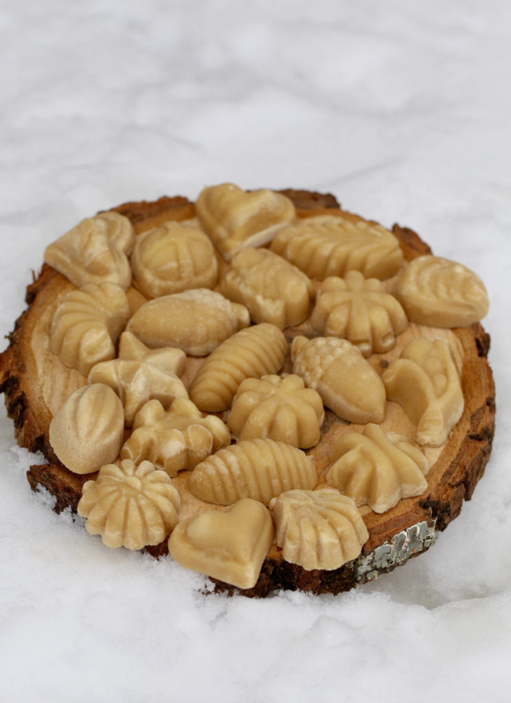 Many pieces of homemade maple candy are decoratively displayed on a tree slice in the snow.