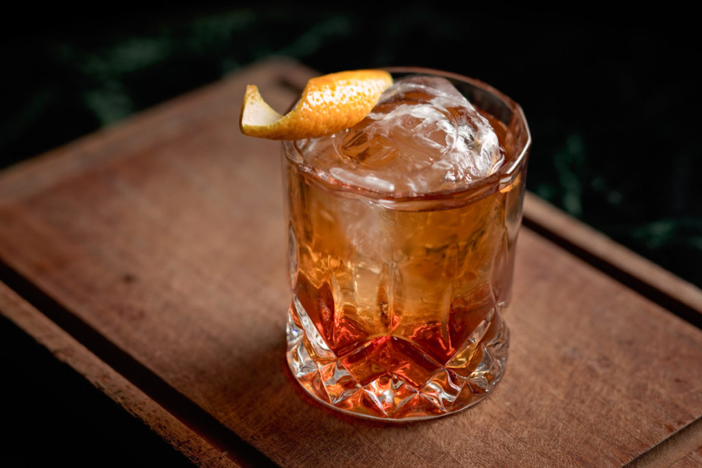 An old fashioned (cocktail) with an orange peel garnish.