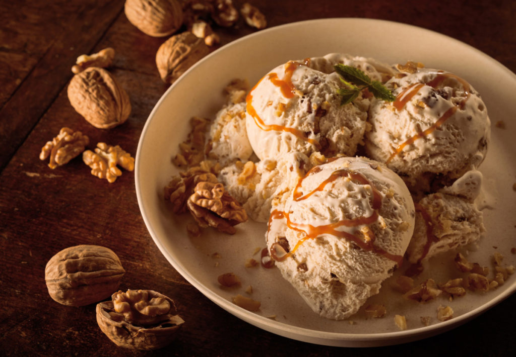 Ice cream in a dish with walnut pieces in the dish and caramel on top.