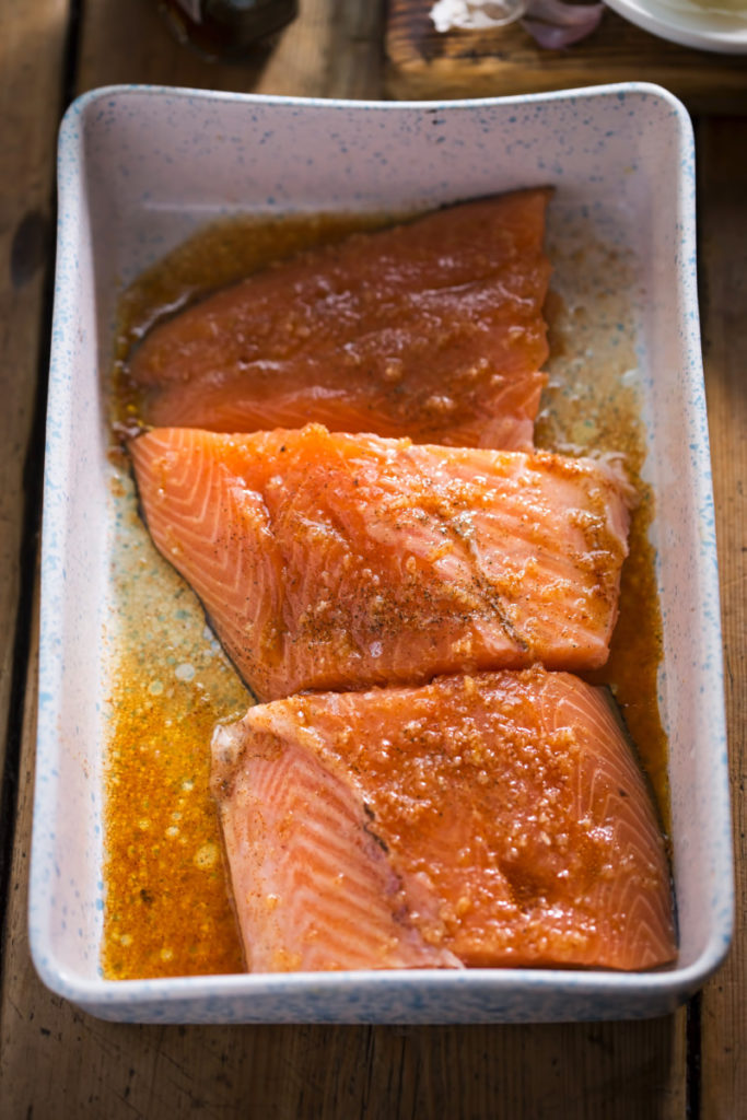 Three salmon planks in a baking dish with a maple syrup marinade poured over them.