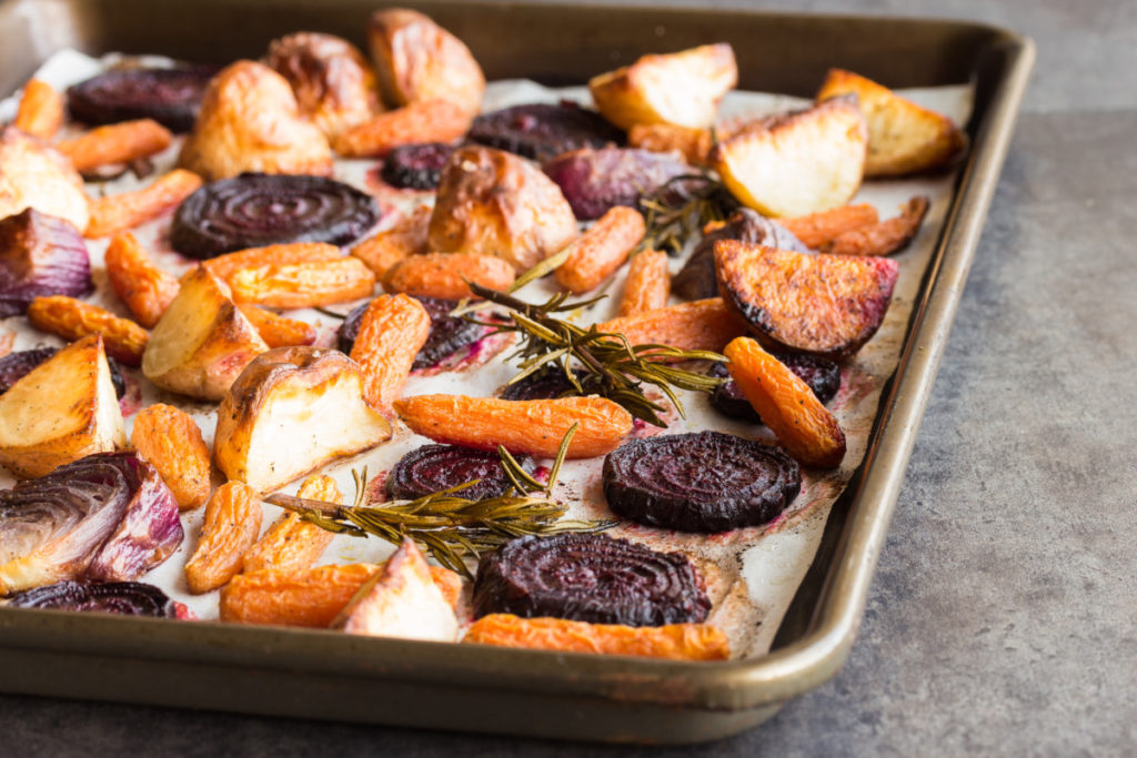 A sheet pan with roasted potatoes, onions, beets, and carrots with rosemary sprigs.