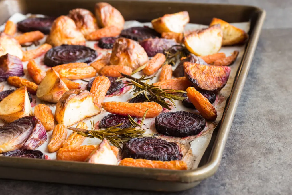A sheet pan with roasted potatoes, onions, beets, and carrots with rosemary sprigs.