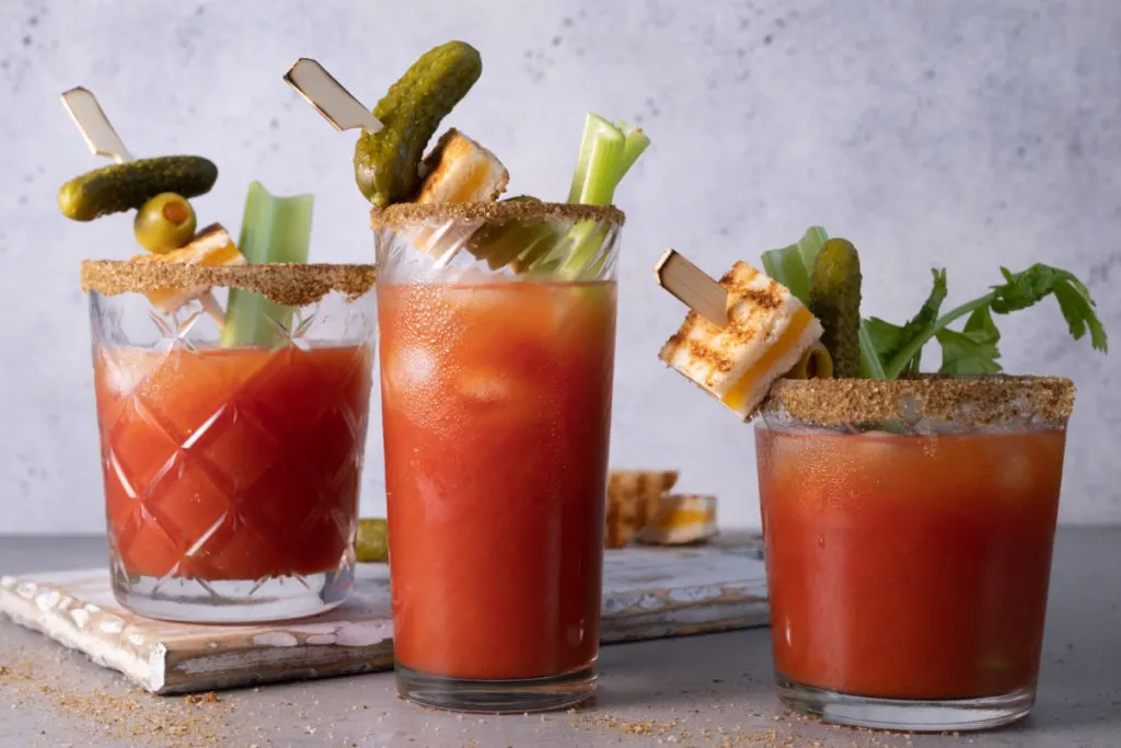 Three bloody mary drinks with fancy garnishes.